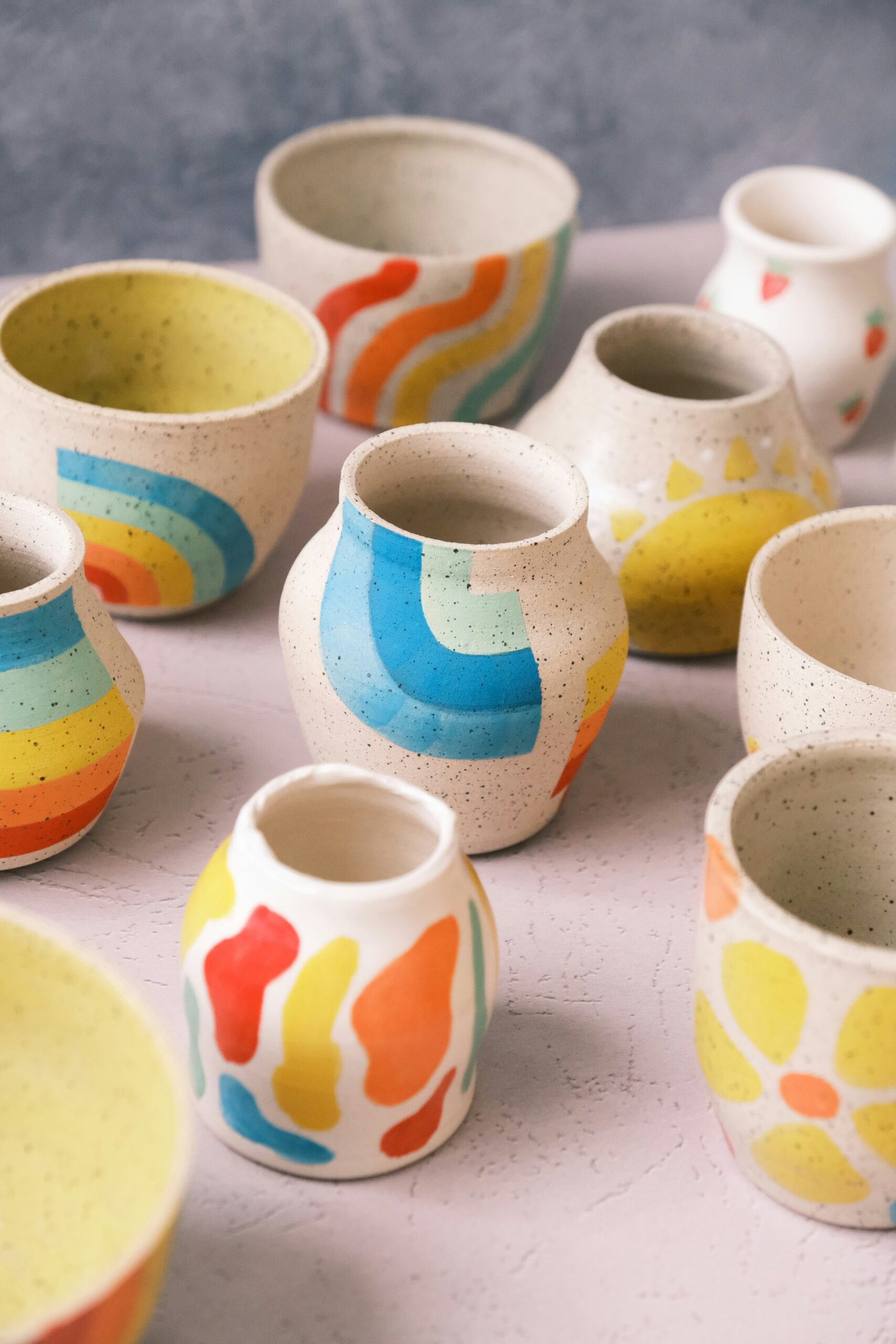 handmade-ceramic-pottery-markers-market-fundraiser Handcrafted ceramic cups and vases decorated with colorful, abstract and geometric designs displayed on a table—perfect examples of the unique, handmade goods often featured at makers market fundraisers.