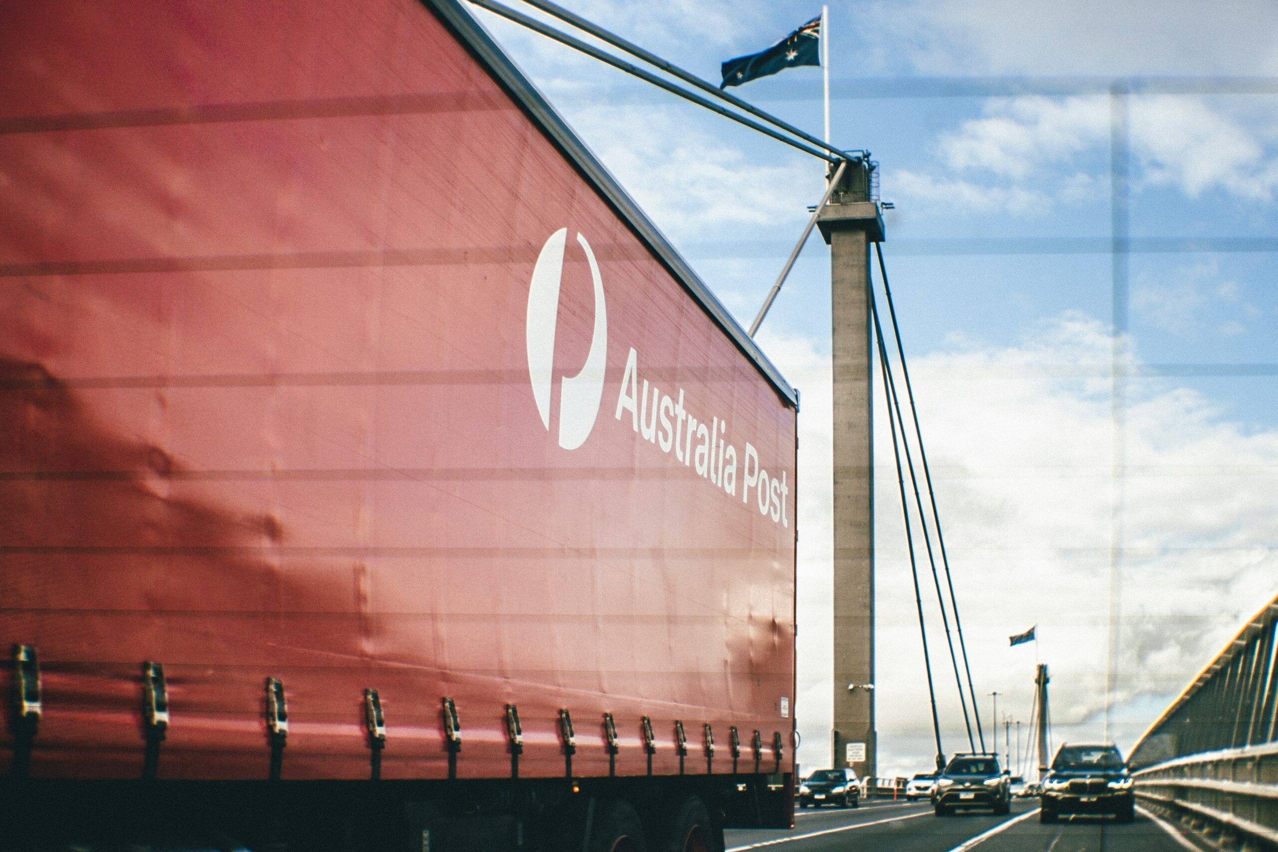 Australia Post delivery truck crossing a bridge under a blue sky with Australian flag flying