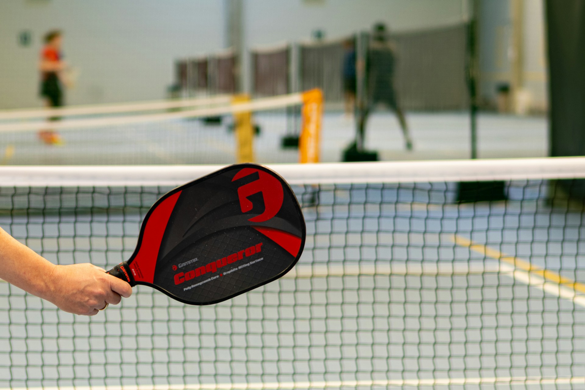 Pickleball paddle held at the net during an indoor tournament game, perfect for peer-to-peer fundraising events